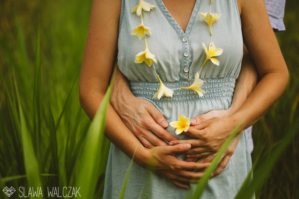 close up photo of a maternity belly and Plumeria girland during an destination engagement, maternity photo session in Ubud's paddy fields in Bali